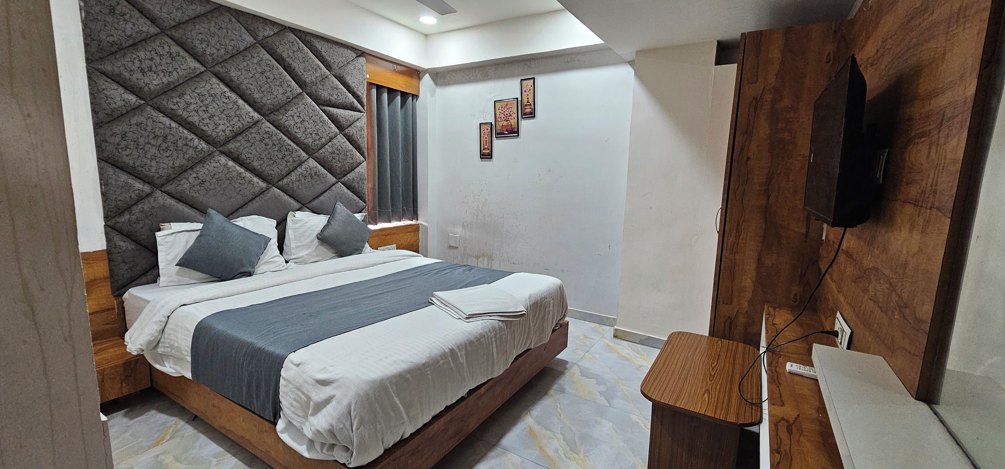 A hotel room with a bed, a wooden headboard, a flat-screen TV, and a small wooden table.
