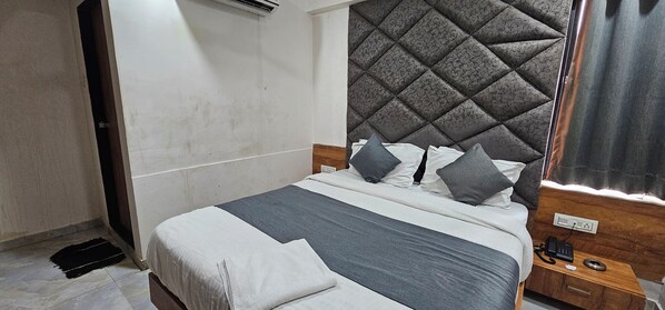 A hotel room with a bed, a bedside table, a telephone, and a power outlet.
