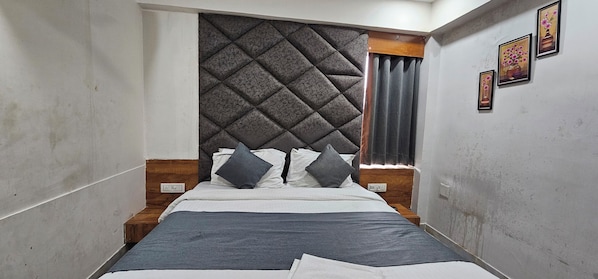 A narrow room with a bed, a headboard, and a window with curtains.