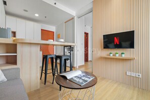 A modern living space with a kitchen, dining area, and a TV mounted on a wooden wall. - Niren by Kozystay - Kuningan (South Jakarta)