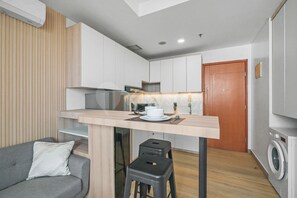 A compact living space with a kitchenette, a dining area, a sofa, and a washing machine. - Niren by Kozystay - Kuningan (South Jakarta)