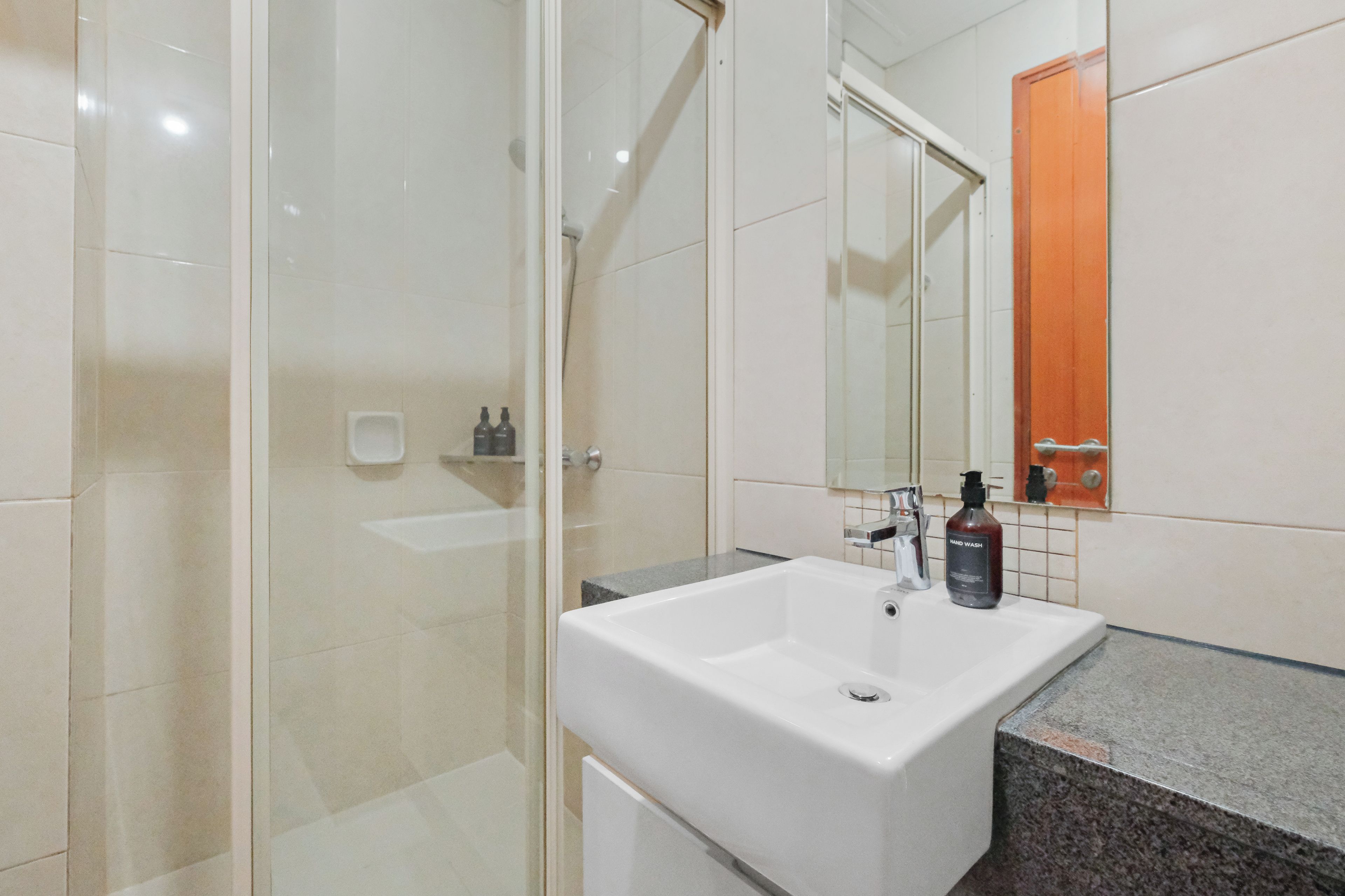 A bathroom with a glass shower enclosure, a white sink, and a mirror with an orange towel rack.