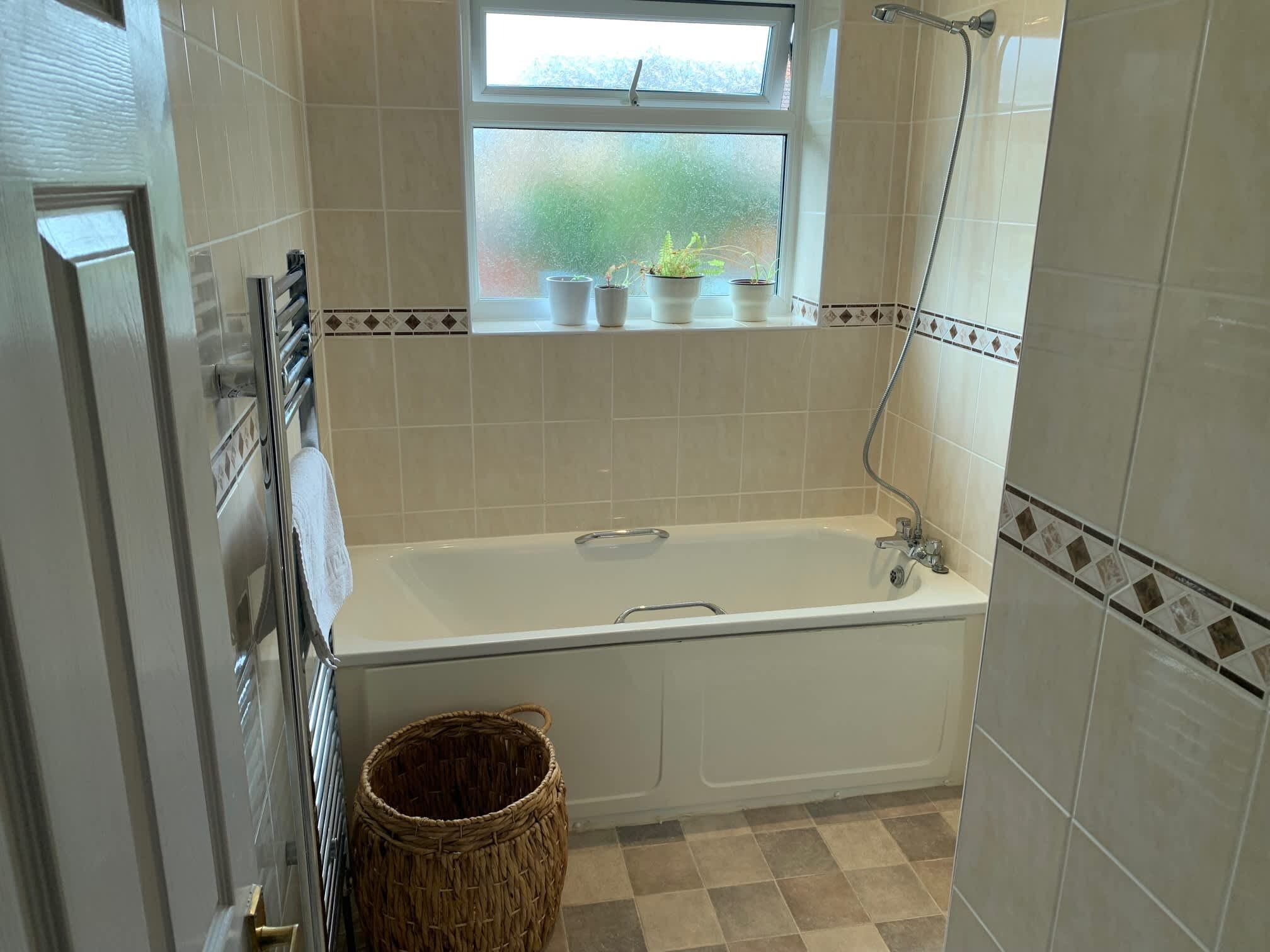 A bathroom with a bathtub, a window with plants, and a shower.