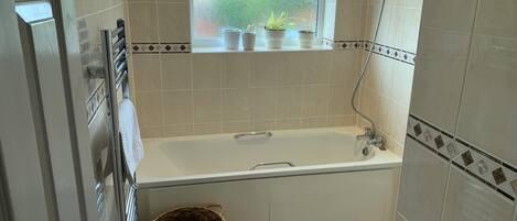 A bathroom with a bathtub, a window with plants, and a shower.