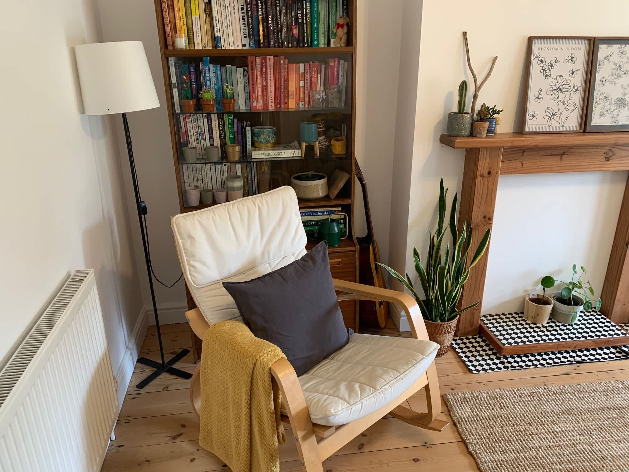 A cozy reading nook with a chair, a bookshelf, a lamp, and a fireplace.