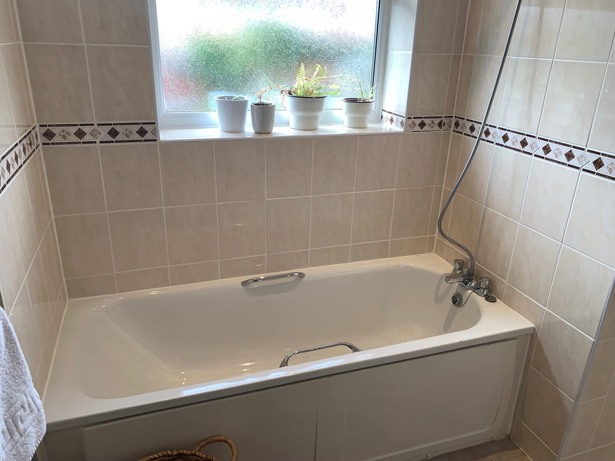 A bathroom with a bathtub, a window with potted plants, and tiled walls.