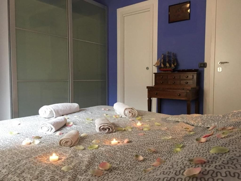 A neatly made bed with rolled towels and candles, a dresser with a ship model, and a blue wall.