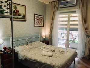 Habitación de hotel con cama, un cuadro, una ventana con cortinas y vistas al balcón.
