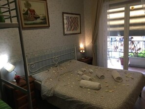Un dormitorio con cama, mesita de noche, lámpara, ventana con cortinas y balcón con barandilla.