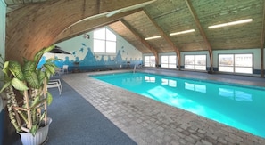 Una piscina interior amb sòl de rajola, bigues de fusta al sostre i un mural a la paret.