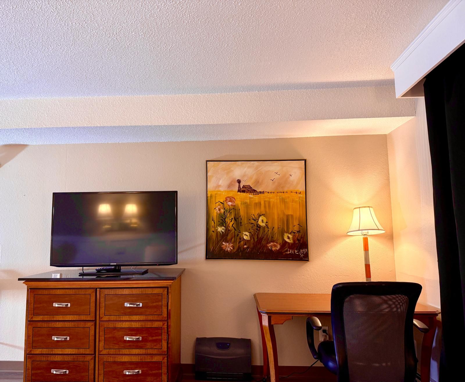 Une chambre d’hôtel équipée d’un téléviseur à écran plat, d’un tableau, d’un bureau, d’une chaise et d’une lampe.