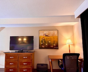 Habitación de hotel con televisión de pantalla plana, un cuadro, un escritorio, una silla y una lámpara.