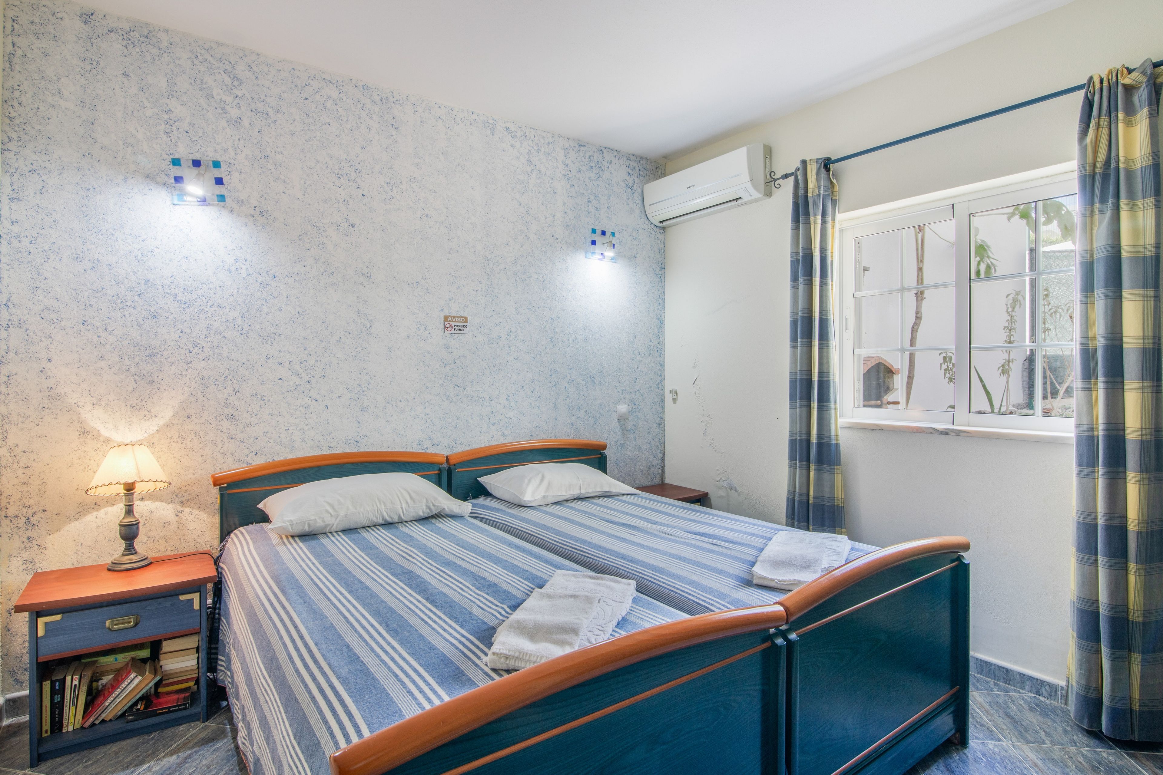 A bedroom with a bed, bedside table, lamp, and a window with curtains.