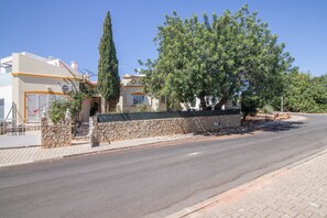 A residential street with houses, a stone wall, and a clear sky.