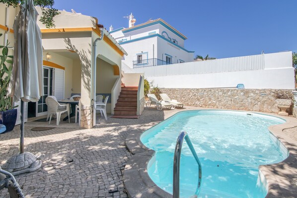 A swimming pool with a stone wall and lounge chairs.