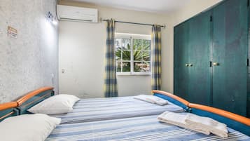 A room with two beds, a window with curtains, a wardrobe, and an air conditioning unit.