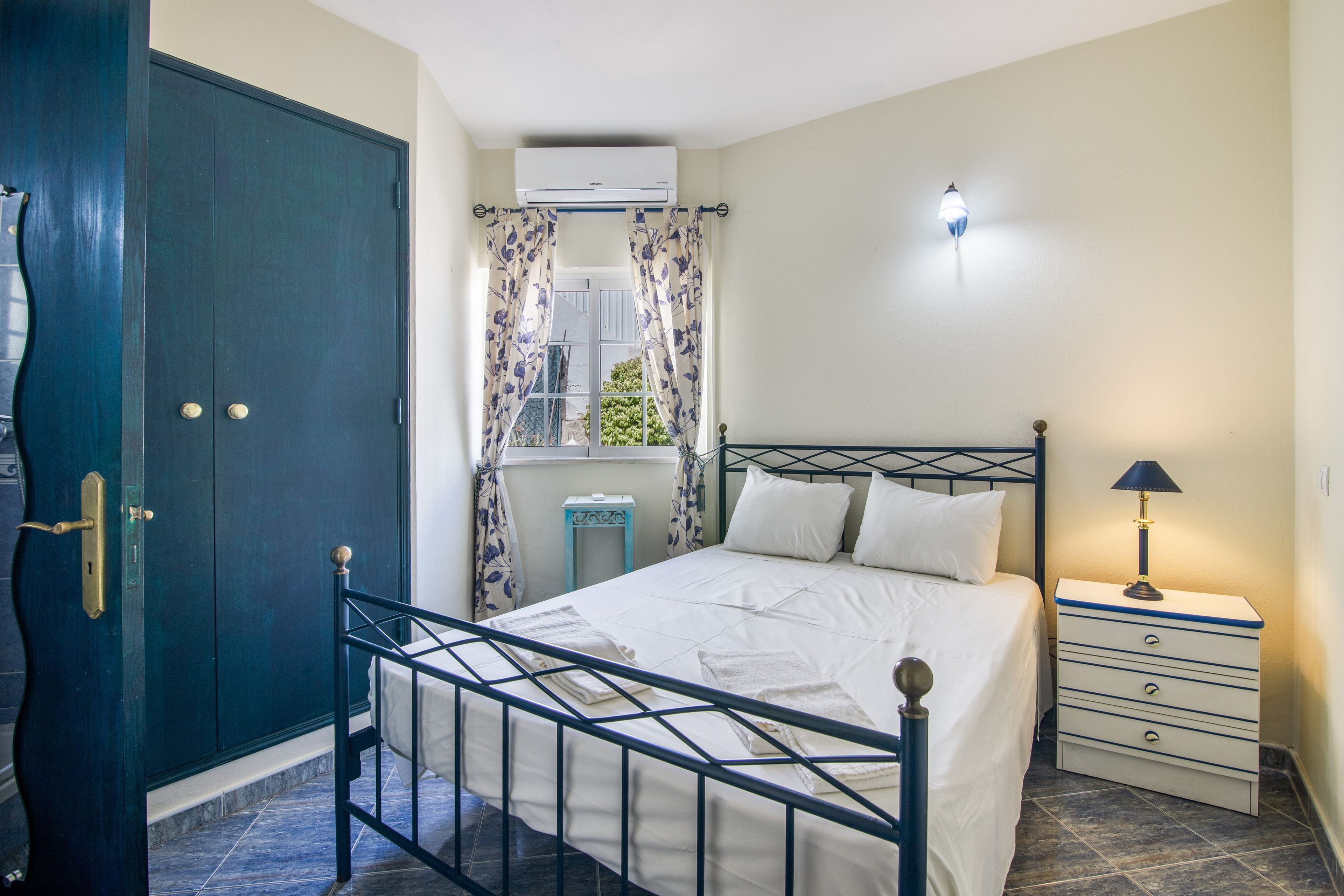 Een slaapkamer met een bed, nachtkastje, lamp en een kledingkast.