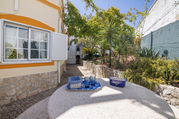 A courtyard with a table set for dining, surrounded by stone walls and various plants.