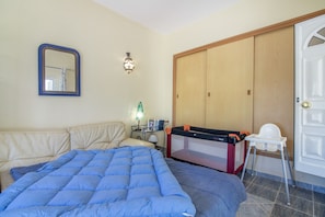 A bedroom with a bed, a sofa, a wardrobe, a lamp, and a baby changing station.