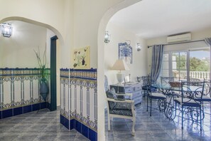 Un área de comedor con una mesa y sillas, un florero con plantas y una pared con azulejos decorativos.