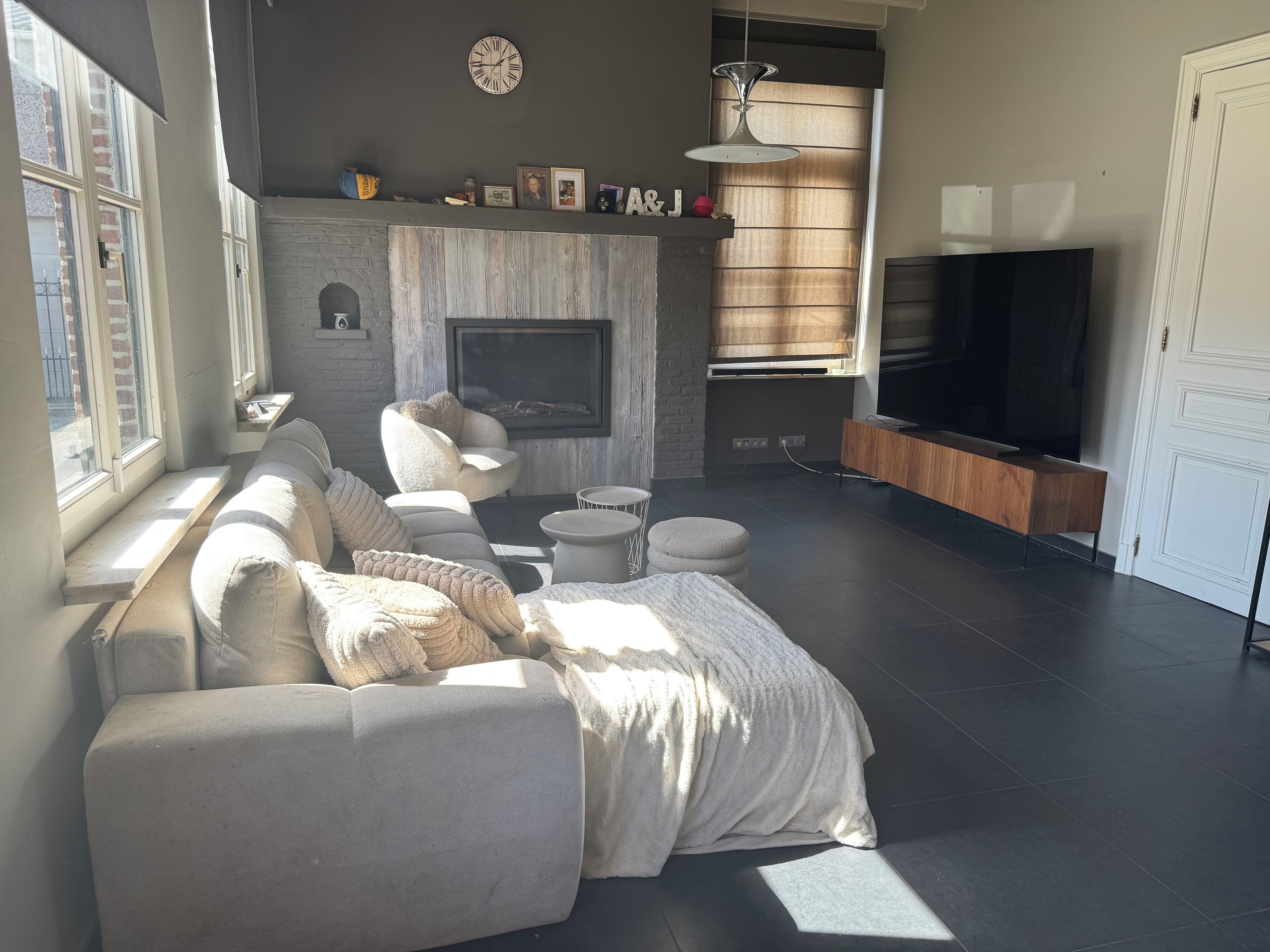 A modern living room with a fireplace, sofa, TV, and a large window.