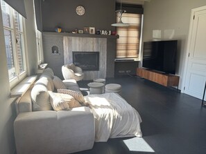 Una sala de estar moderna con chimenea, sofá, televisor y un ventanal grande.