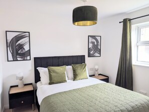 Un dormitorio moderno con cama, dos mesitas de noche, una lámpara de pared y arte abstracto.