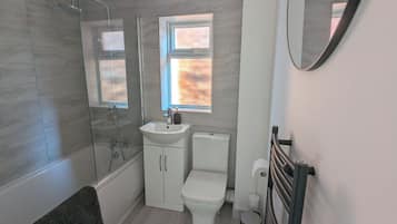 A modern bathroom with a glass shower enclosure, a white sink, a toilet, and a towel rack.