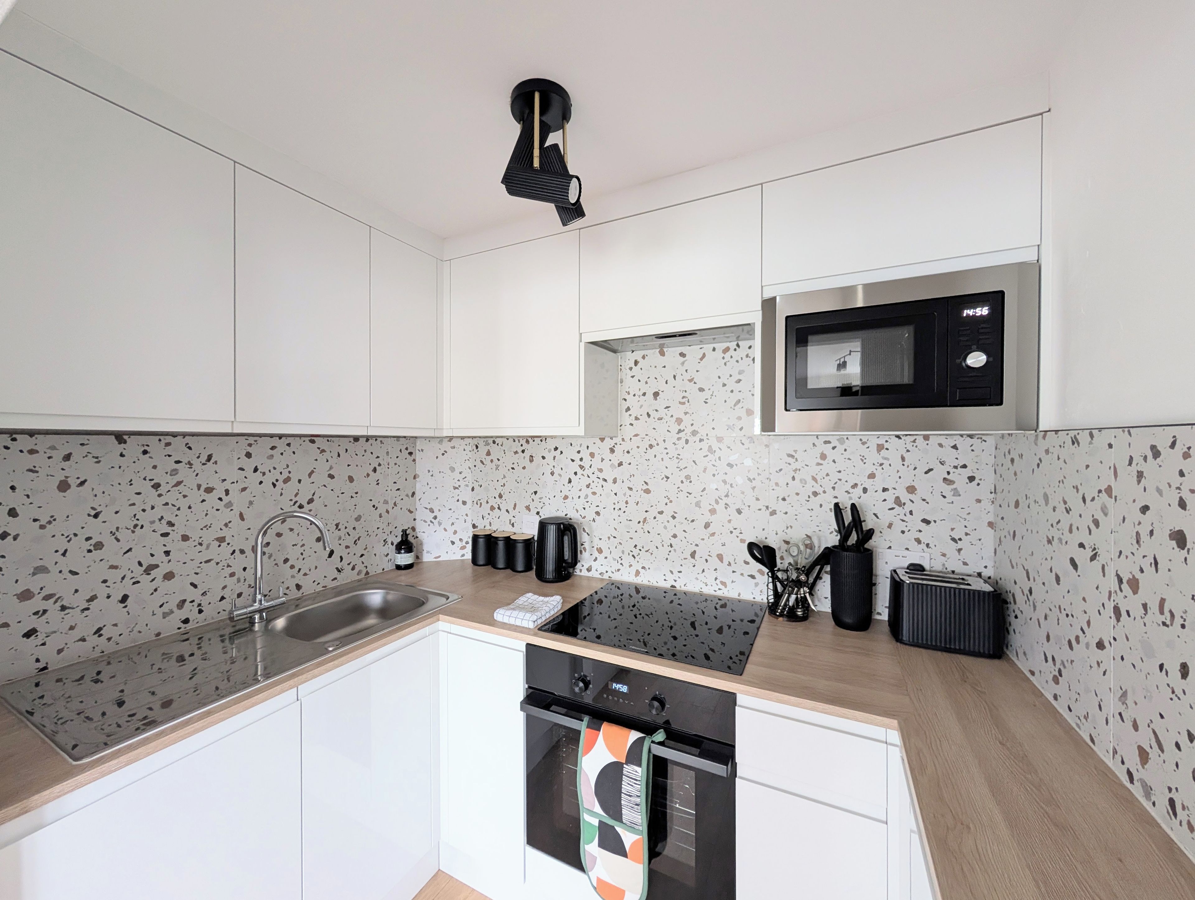 Cozinha moderna com armários brancos, pia de aço inoxidável, micro-ondas e lava-louças.