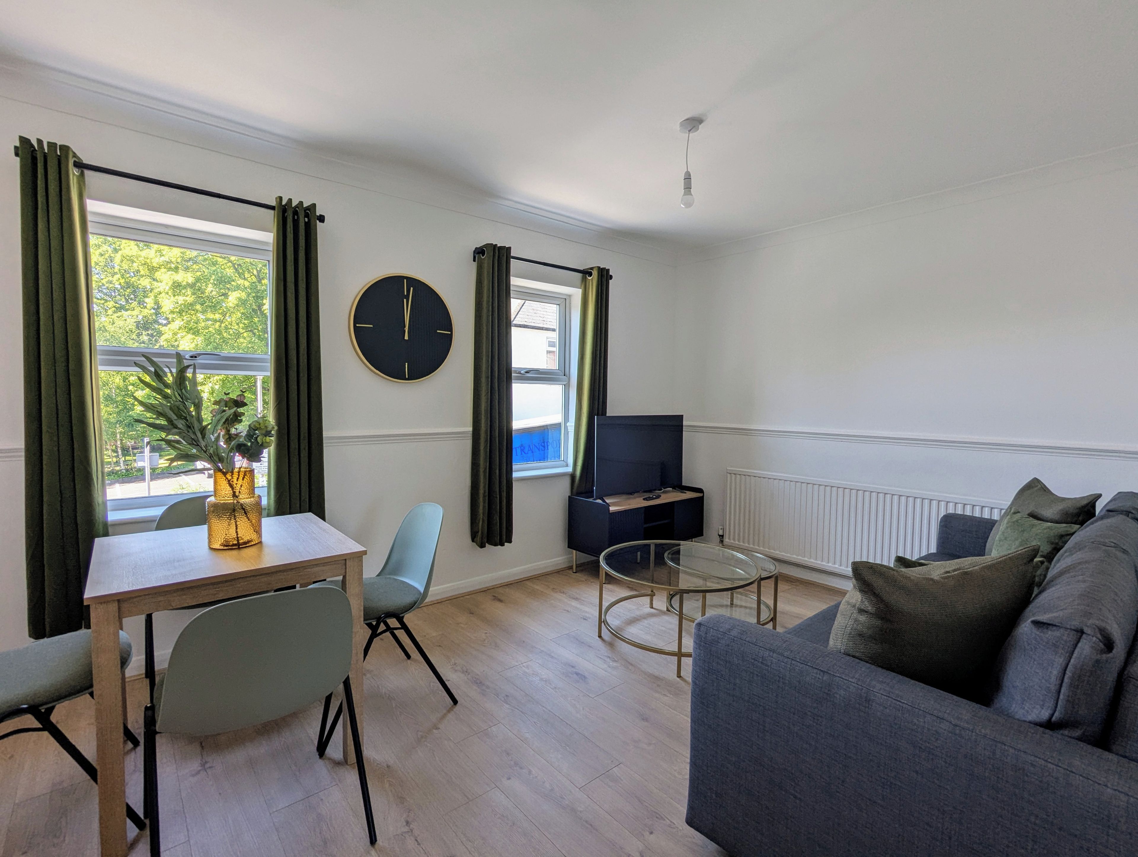 Uma sala de estar moderna com sofá, mesa de jantar com cadeiras, rack para TV e uma janela grande com cortinas.