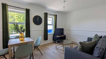 Uma sala de estar moderna com sofá, mesa de jantar com cadeiras, rack para TV e uma janela grande com cortinas.