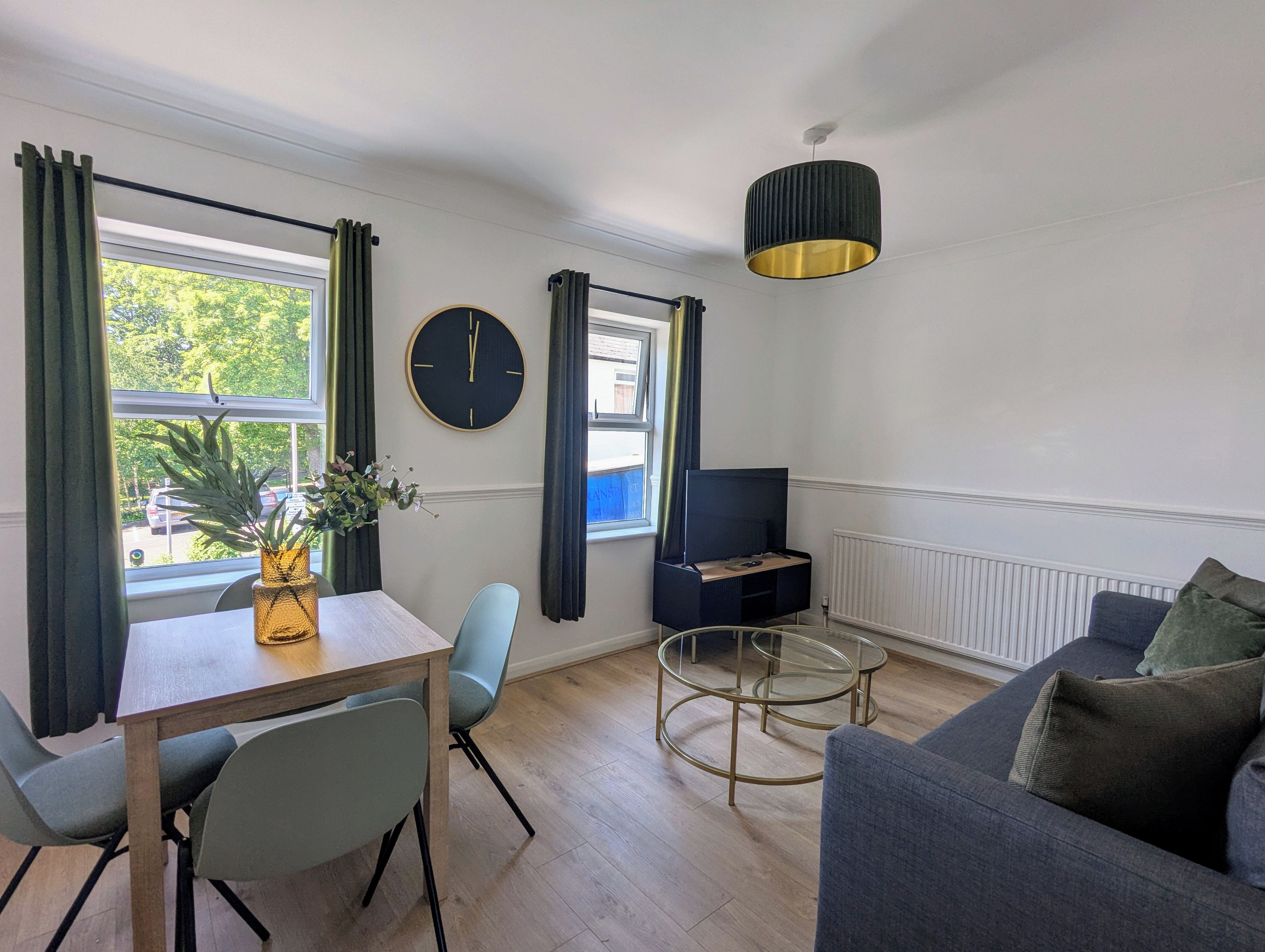 Un salon moderne comprenant un coin repas, un téléviseur et une grande fenêtre avec des rideaux.
