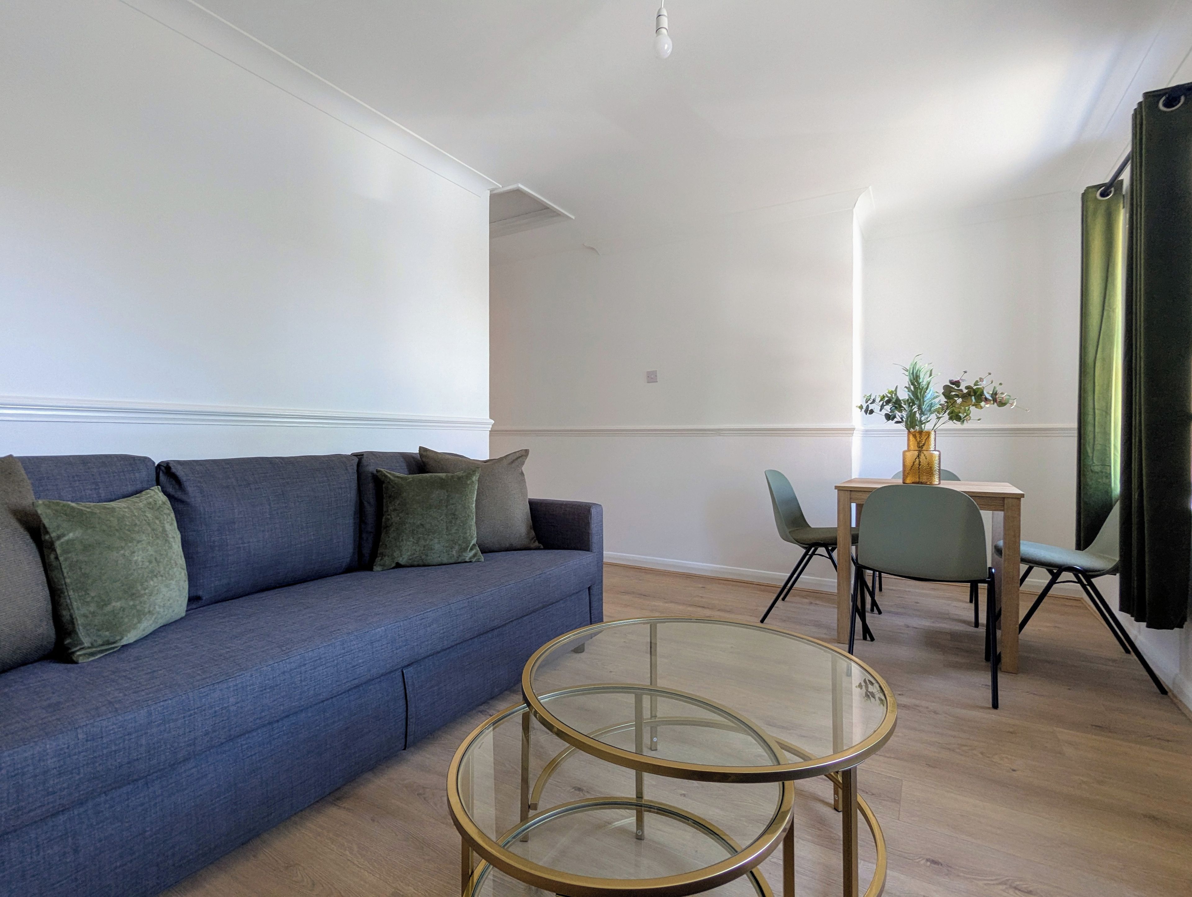 A modern living room with a blue sofa, two glass-top coffee tables, and a small dining table with chairs.