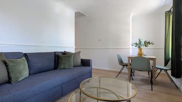 A modern living room with a blue sofa, two glass-top coffee tables, and a small dining table with chairs.