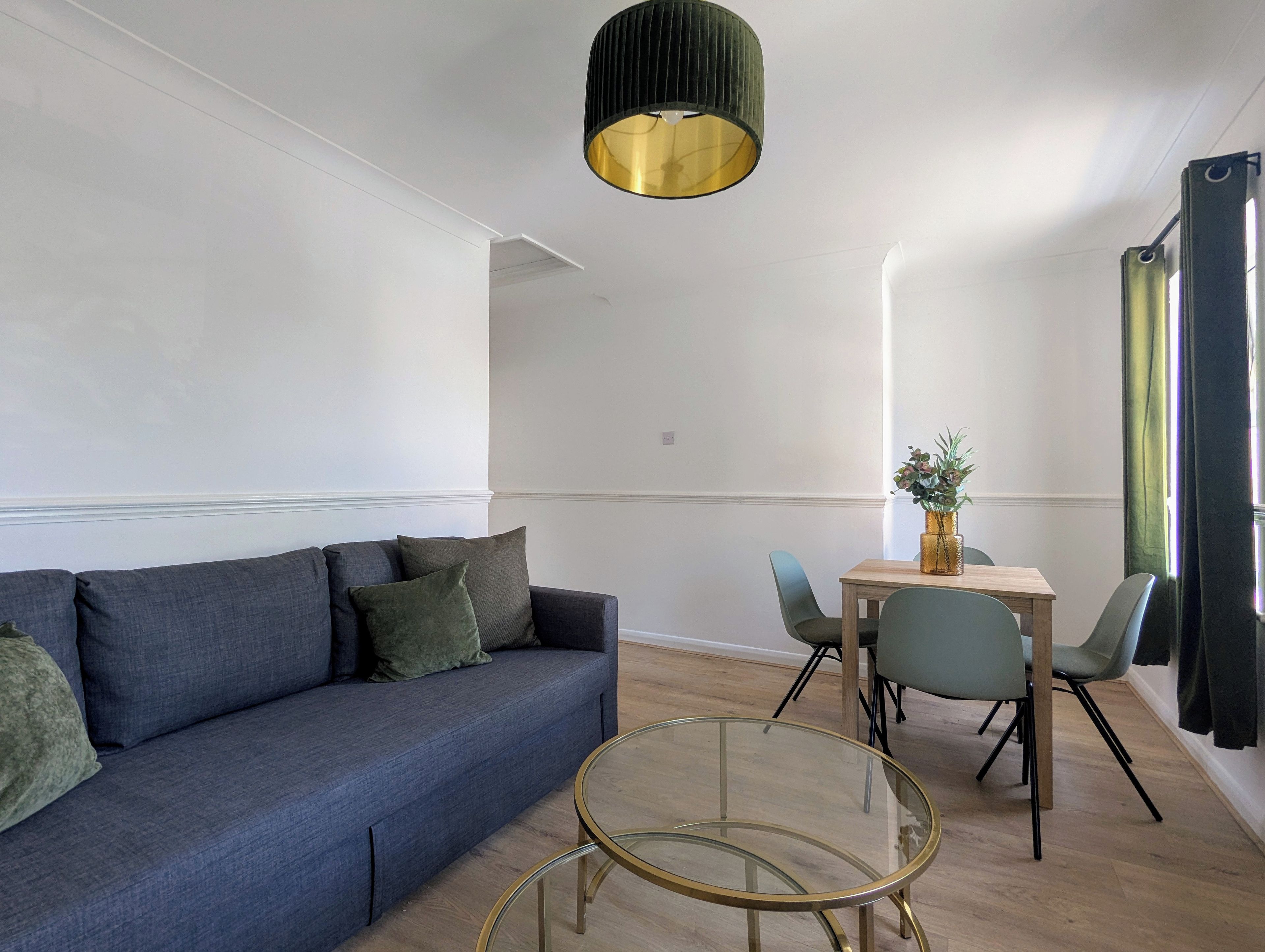 A modern living room with a blue sofa, a glass coffee table, and a dining area with a wooden table and chairs.