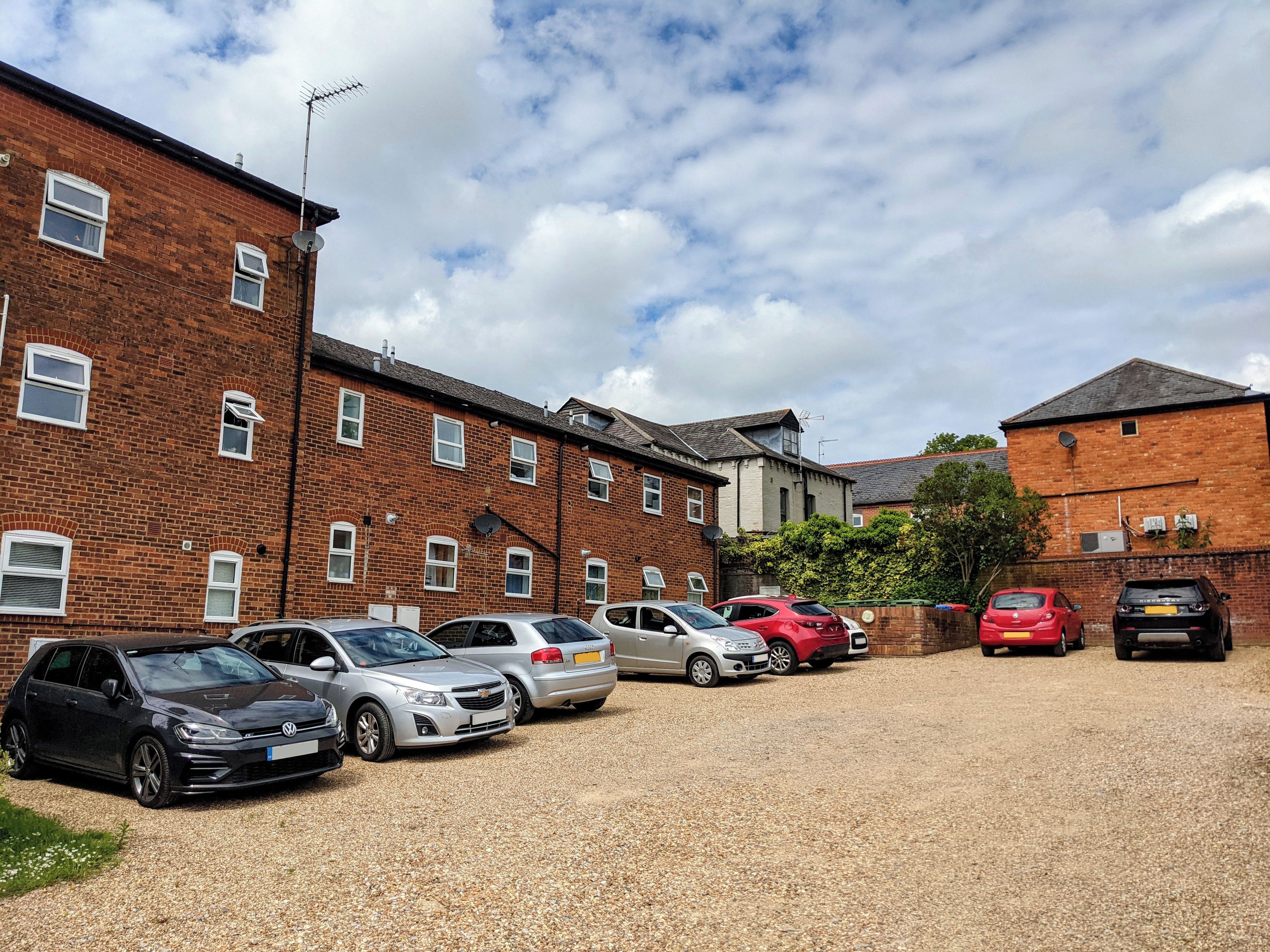 A parking area with several cars and a building with brick walls and multiple windows.