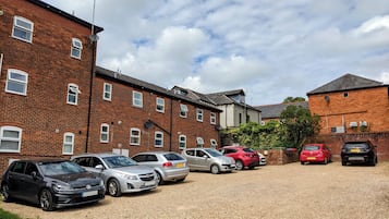A parking area with several cars and a building with brick walls and multiple windows.