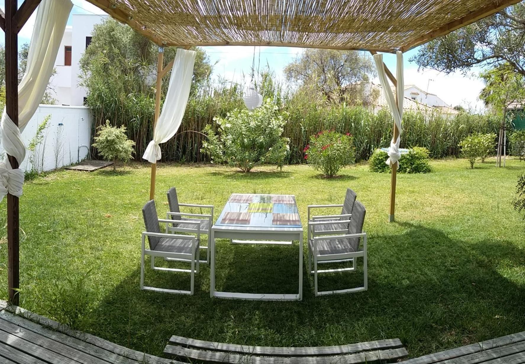 Een terras buiten met een tafel en stoelen, omgeven door een gazon en verschillende planten.
