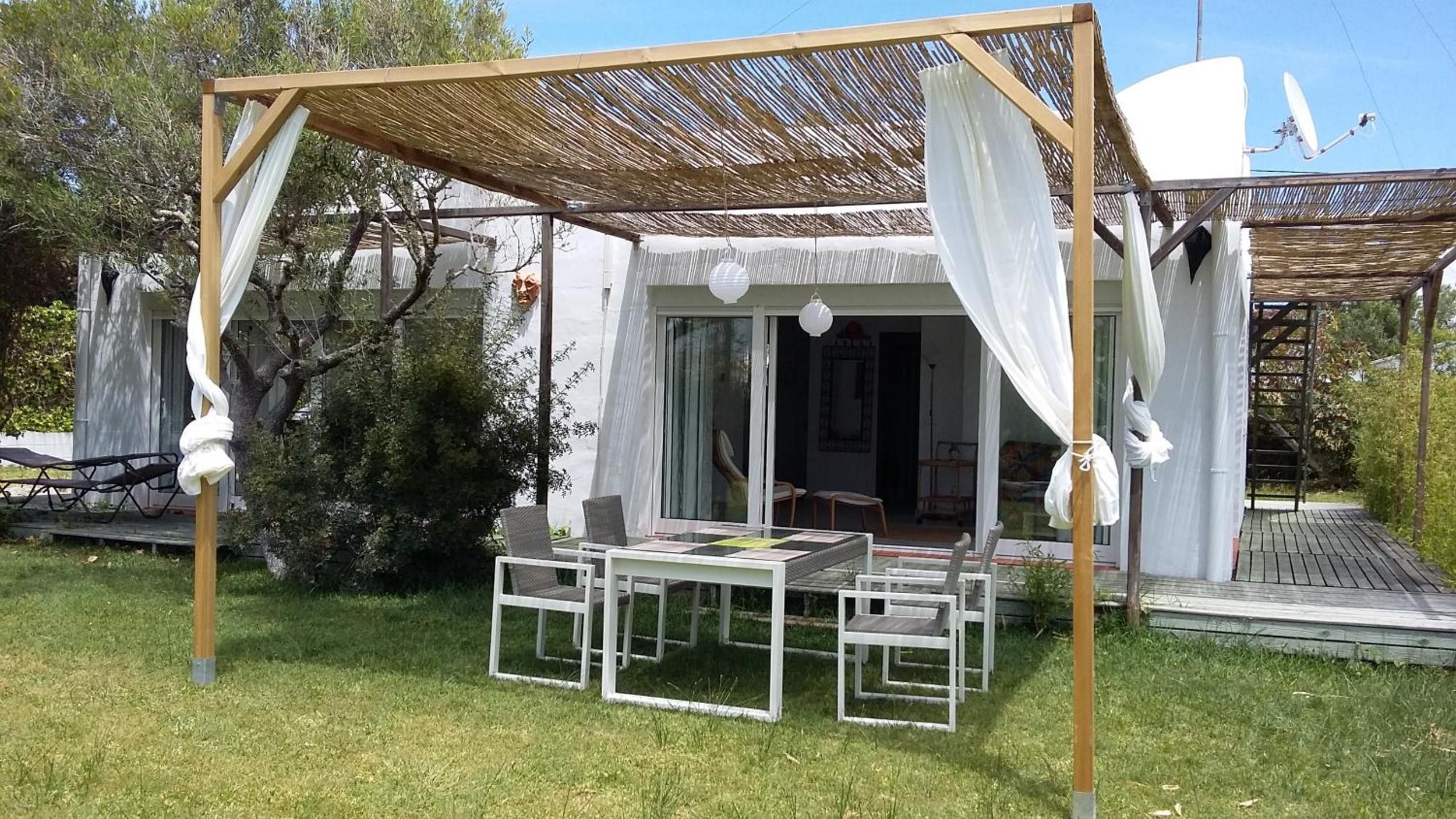 An outdoor patio with a table and chairs, a pergola with a white canopy, and a building with a glass door.