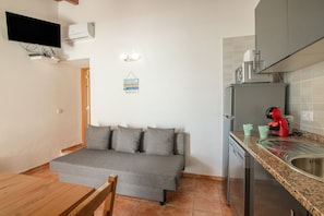 A compact living space with a sofa, a dining table, a kitchenette, and a flat-screen TV mounted on the wall.