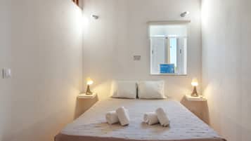 Habitación de hotel estrecha con cama, dos lámparas de noche, ventana con vistas y una mesita de noche pequeña.