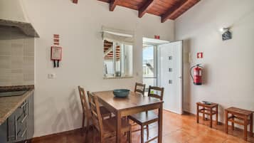 A dining area with a wooden table and chairs, a fire extinguisher mounted on the wall, and a window with a view of the outside.