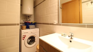 Une petite salle de bain équipée d’un lave-linge, d’un évier et d’un miroir.
