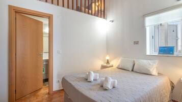 Een slaapkamer met een bed, een nachtkastje, een raam met jaloezieën, een deur en een trap.