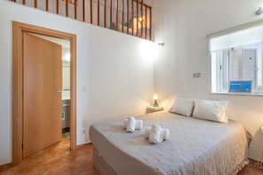 A bedroom with a bed, a nightstand, a window with blinds, a door, and a staircase.