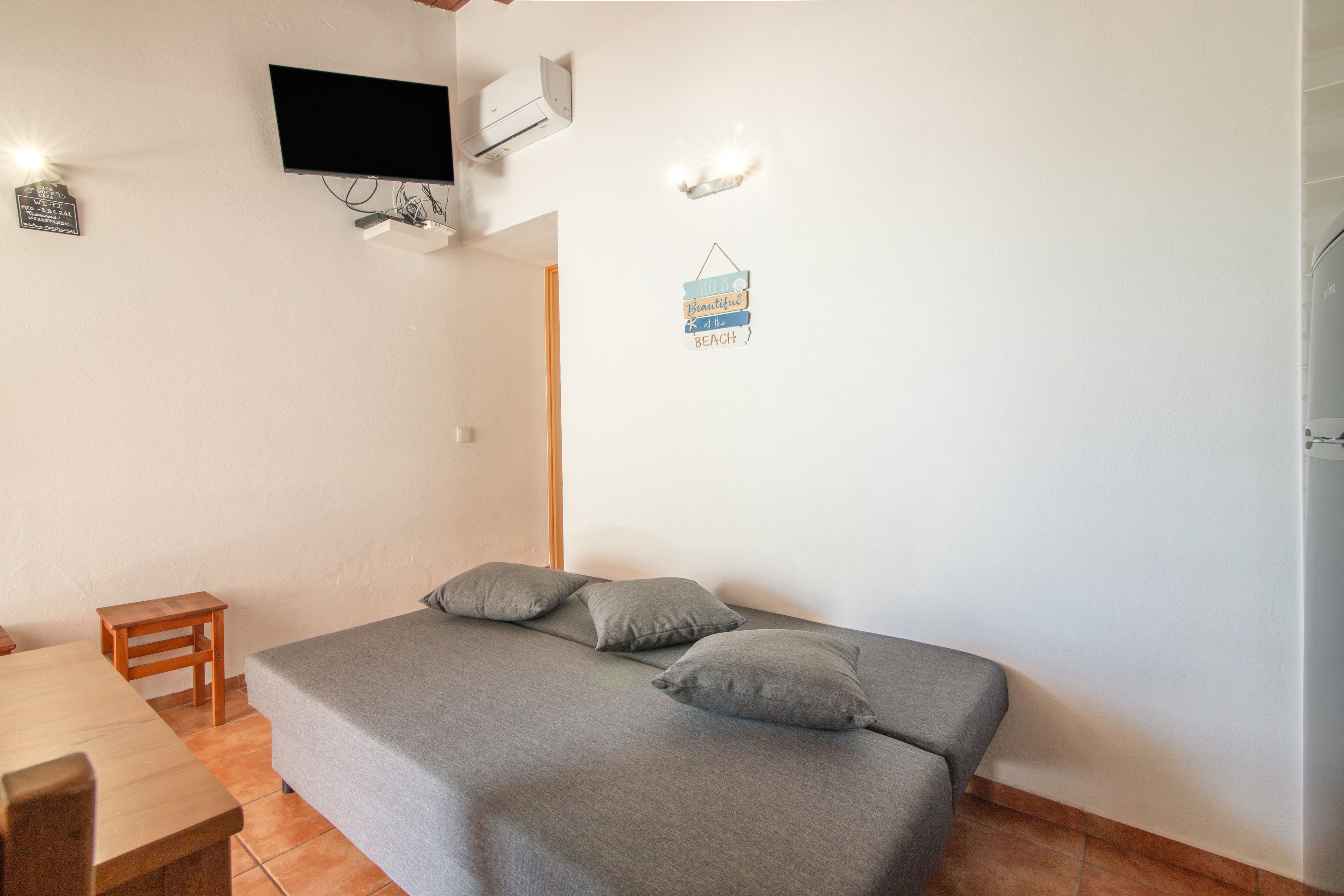 Ein Schlafzimmer mit einem Bett, einem an der Wand befestigten Fernseher und einem kleinen Tisch.