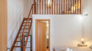 A bedroom with a wooden staircase, a bed with white bedding, and a bedside lamp.