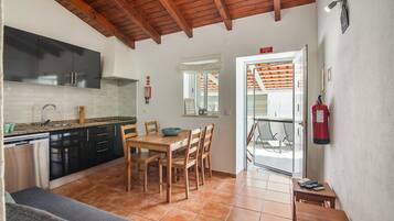 Cocina compacta con electrodomésticos modernos, zona de comedor con mobiliario de madera y señal de salida de emergencia visible.