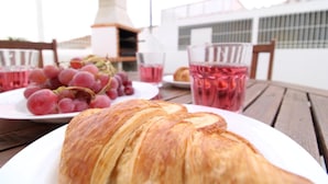 Une table avec un croissant, une assiette de raisins et un verre d’une boisson rose.
