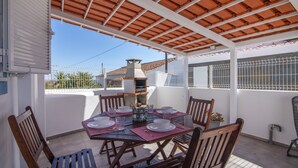 A covered patio area with a table set for dining, a barbecue grill, and a view of the surrounding area.